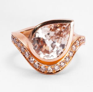 Geschwungerner Ring in Rosegold mit hellbraunem Zirkon in Tropfenform und hellbraunen Diamanten am unteren Rand.